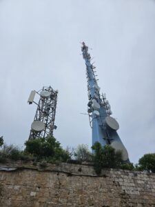 Zwei Funktürme hinter einer Steinmauer bei bewölktem Himmel